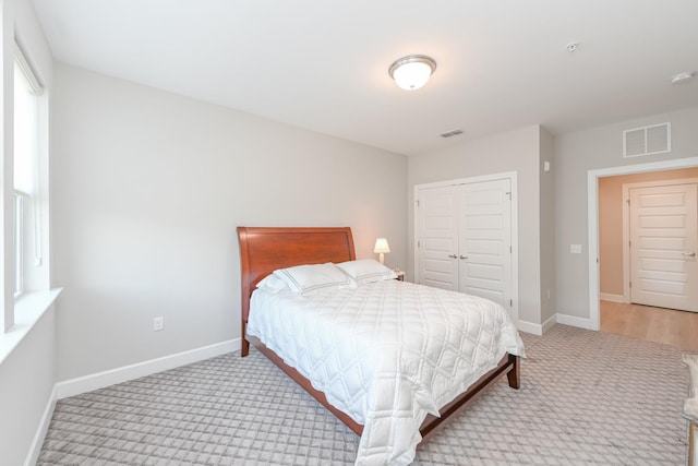 bedroom with light colored carpet, visible vents, a closet, and baseboards