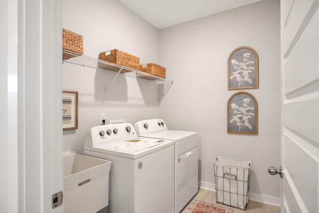 laundry area with light wood finished floors, washing machine and dryer, a sink, laundry area, and baseboards