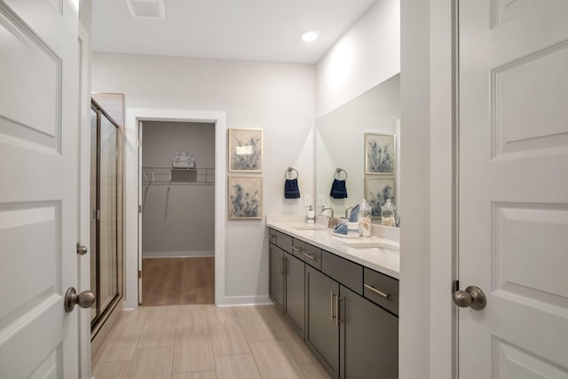 bathroom featuring double vanity, a stall shower, visible vents, a walk in closet, and a sink