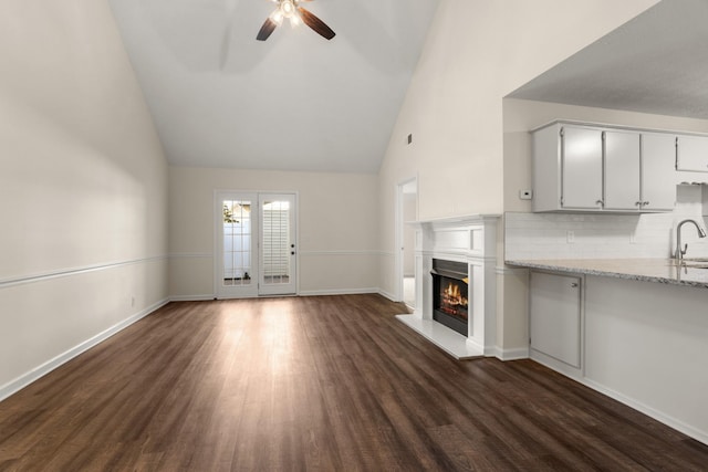 unfurnished living room featuring a sink, dark wood finished floors, a ceiling fan, baseboards, and a glass covered fireplace