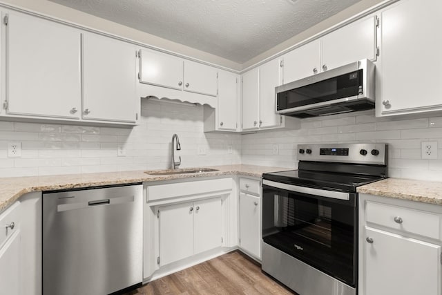 kitchen featuring decorative backsplash, light wood-style flooring, stainless steel appliances, a textured ceiling, and a sink