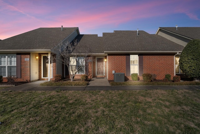 back of property at dusk featuring a yard, brick siding, and central air condition unit