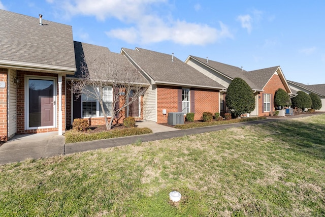 single story home with central AC unit, brick siding, a front yard, and a shingled roof