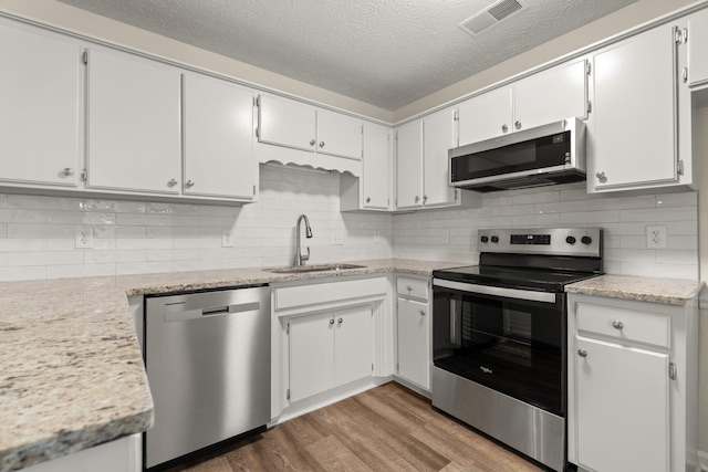 kitchen featuring stainless steel appliances, visible vents, backsplash, a sink, and wood finished floors