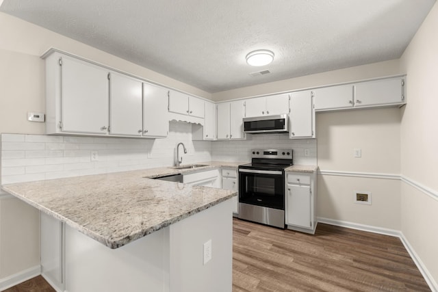 kitchen featuring visible vents, appliances with stainless steel finishes, wood finished floors, a peninsula, and a sink