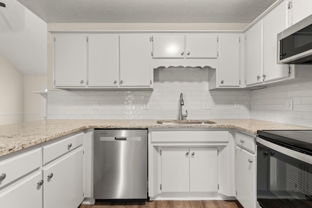 kitchen featuring a textured ceiling, light stone countertops, a sink, appliances with stainless steel finishes, and decorative backsplash