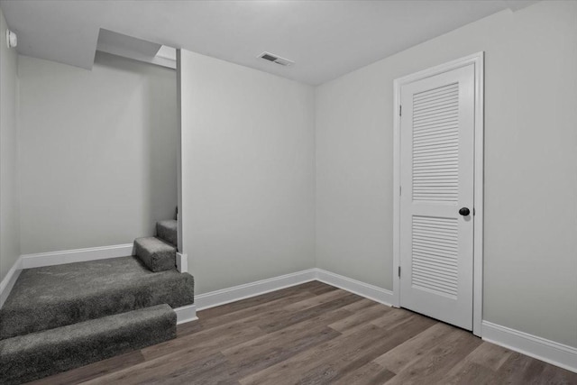 empty room featuring wood finished floors, visible vents, baseboards, and stairs