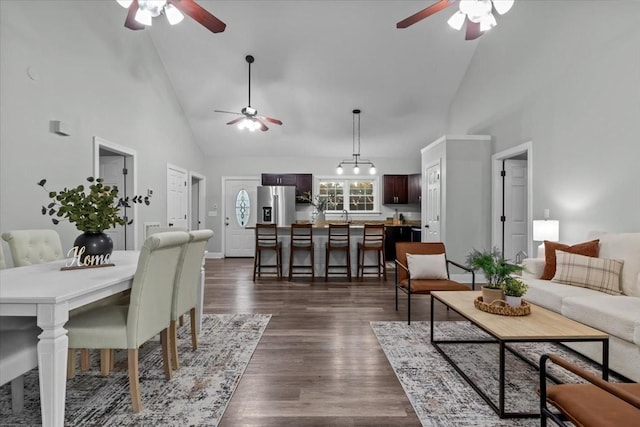 living area with high vaulted ceiling, dark wood-type flooring, a ceiling fan, and baseboards