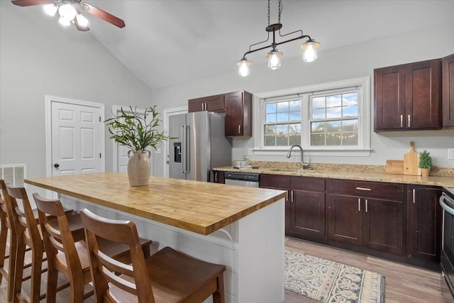 kitchen with appliances with stainless steel finishes, a breakfast bar, vaulted ceiling, and a sink