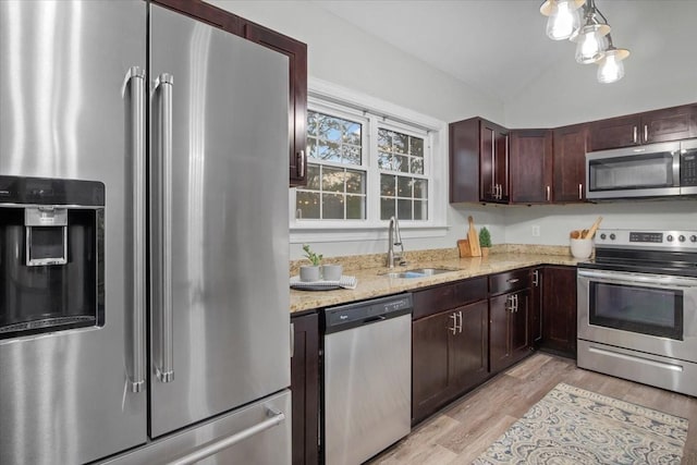 kitchen featuring light wood-style flooring, appliances with stainless steel finishes, light stone countertops, vaulted ceiling, and a sink