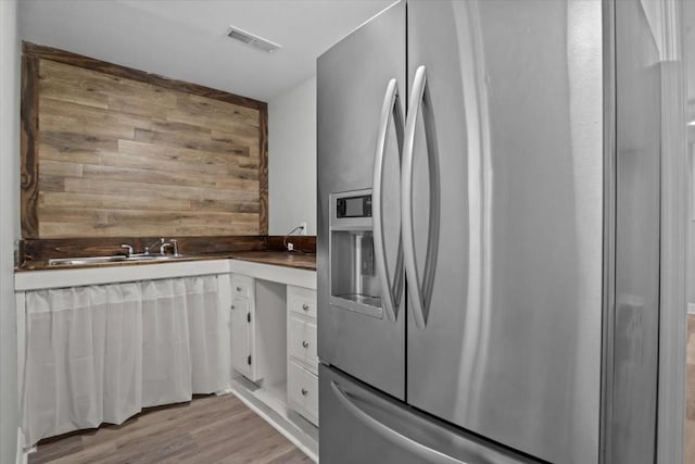 kitchen featuring a sink, visible vents, white cabinets, light wood-style floors, and stainless steel fridge with ice dispenser