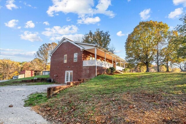 view of side of property featuring french doors, gravel driveway, a yard, central AC, and brick siding