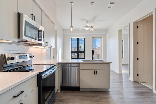 kitchen featuring decorative backsplash, wood finished floors, a peninsula, stainless steel appliances, and a sink