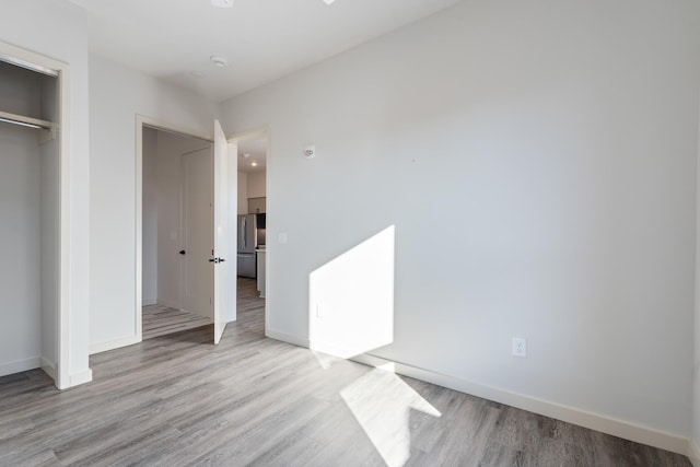 unfurnished bedroom with freestanding refrigerator, a closet, baseboards, and wood finished floors