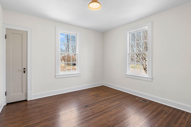 spare room with dark wood-type flooring, visible vents, and baseboards