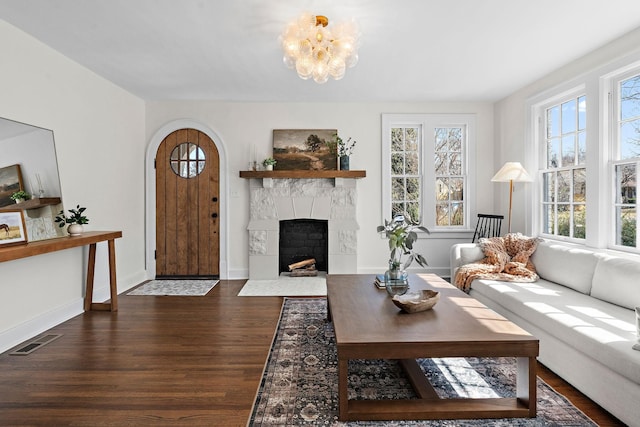 living room featuring arched walkways, a fireplace with flush hearth, wood finished floors, visible vents, and baseboards