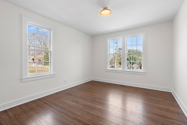 unfurnished room featuring dark wood-style flooring, plenty of natural light, visible vents, and baseboards