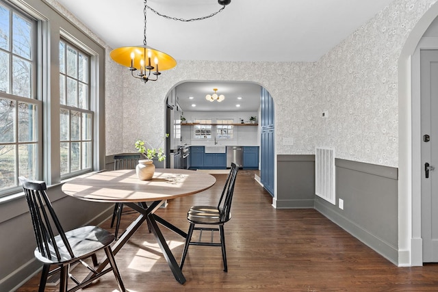 dining space with arched walkways, a notable chandelier, visible vents, wainscoting, and dark wood-style floors