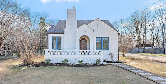 english style home featuring brick siding, fence, a chimney, and roof with shingles