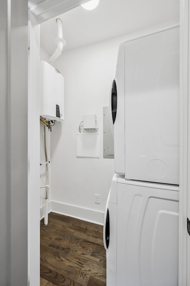 clothes washing area with stacked washer / drying machine, water heater, wood finished floors, laundry area, and baseboards