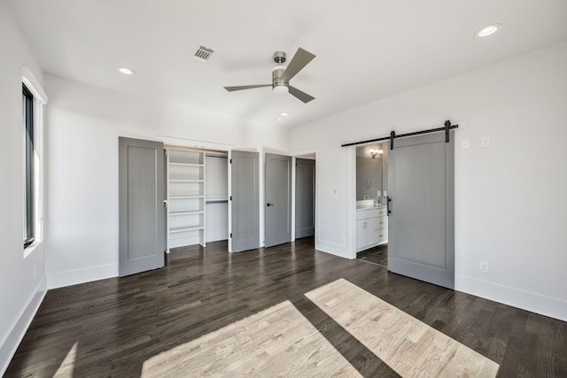 unfurnished bedroom with a barn door, dark wood-type flooring, visible vents, and recessed lighting