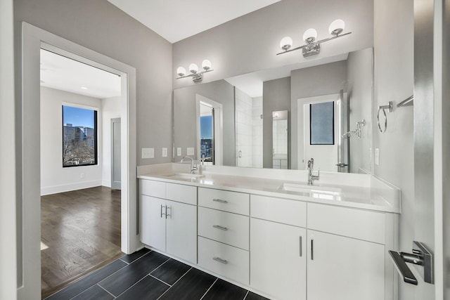 bathroom featuring double vanity, wood finished floors, a sink, and baseboards