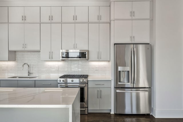 kitchen featuring light stone counters, dark wood finished floors, tasteful backsplash, appliances with stainless steel finishes, and a sink