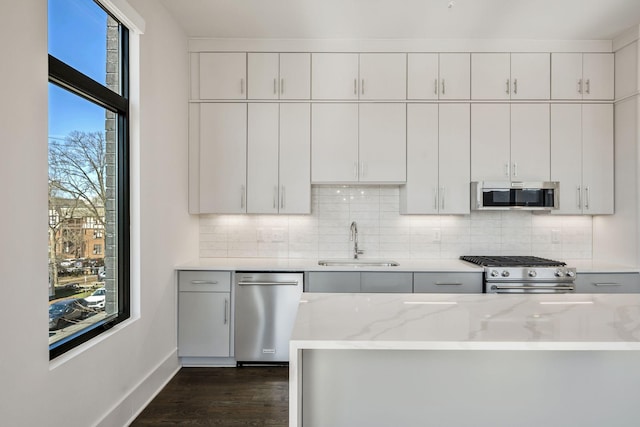 kitchen featuring tasteful backsplash, dark wood finished floors, appliances with stainless steel finishes, light stone counters, and a sink