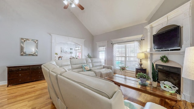 living area with high vaulted ceiling, light wood finished floors, a fireplace, and a ceiling fan