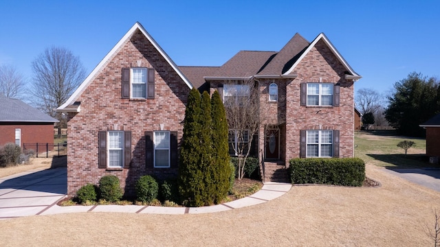 view of front facade with brick siding, roof with shingles, and fence