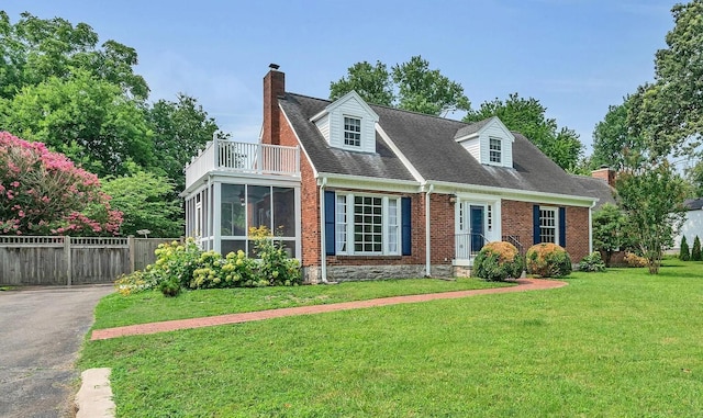 cape cod-style house with brick siding, a balcony, a chimney, fence, and a front yard