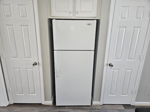 kitchen with dark wood-style floors, baseboards, freestanding refrigerator, and white cabinetry