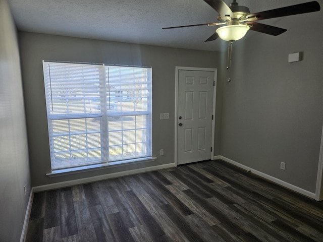 spare room featuring a textured ceiling, dark wood finished floors, and baseboards