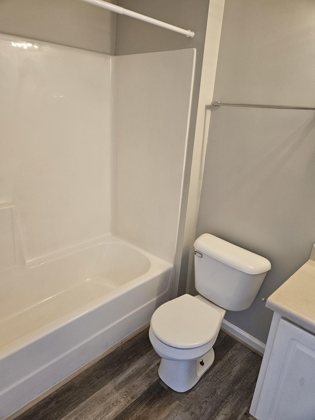 bathroom with toilet, wood finished floors, vanity, bathing tub / shower combination, and baseboards