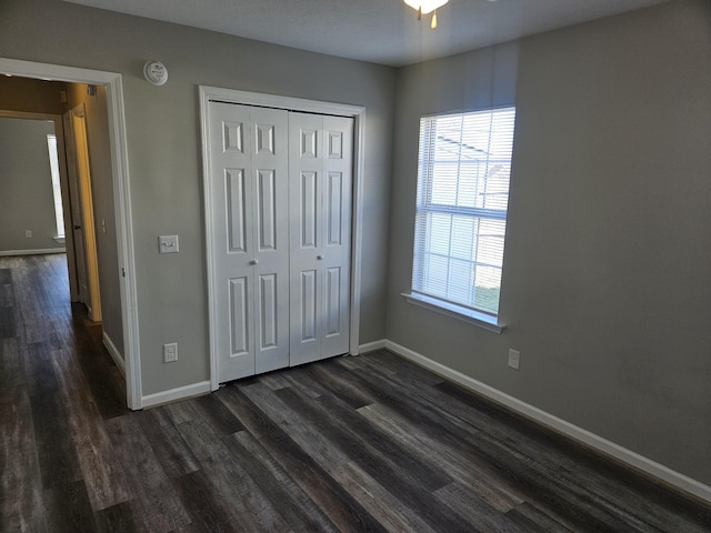 unfurnished bedroom featuring dark wood-style floors, baseboards, and a closet