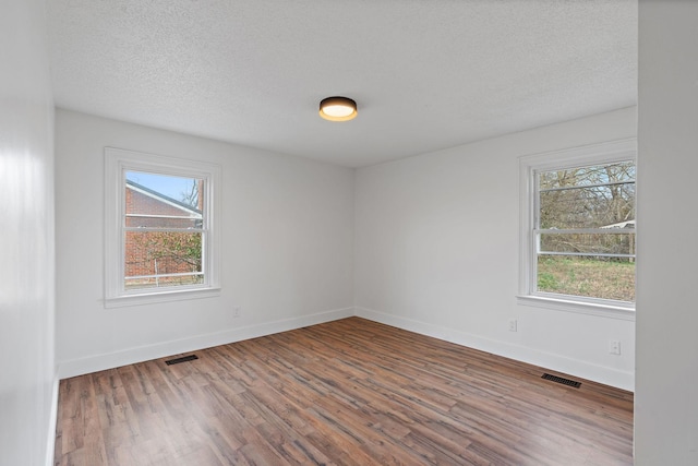 empty room featuring a wealth of natural light, wood finished floors, visible vents, and baseboards