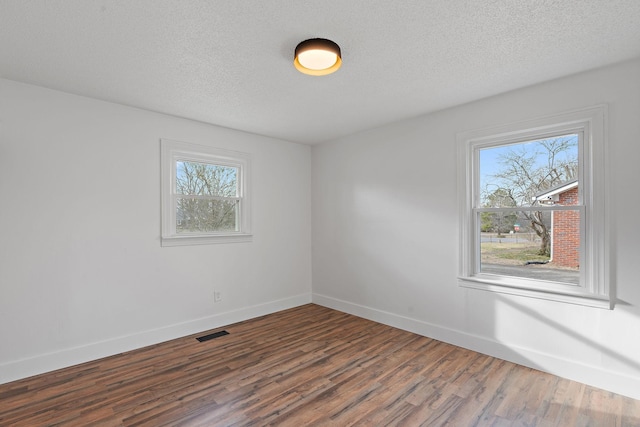 empty room featuring a textured ceiling, wood finished floors, visible vents, and baseboards