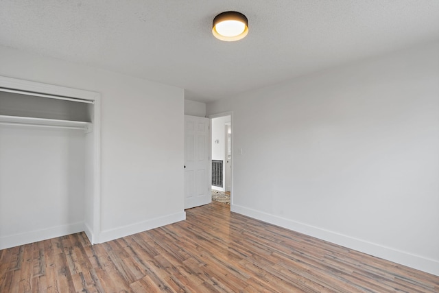 unfurnished bedroom with a textured ceiling, a closet, baseboards, and wood finished floors