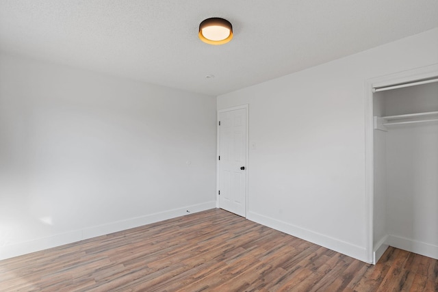 unfurnished bedroom with a closet, a textured ceiling, baseboards, and wood finished floors