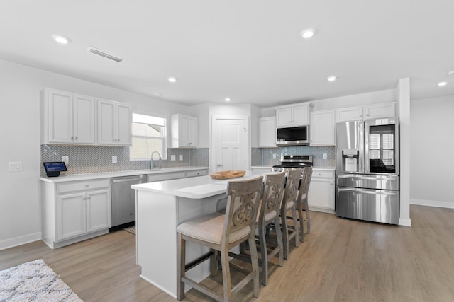 kitchen with stainless steel appliances, a kitchen island, white cabinets, light countertops, and light wood-type flooring