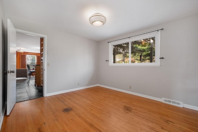 spare room with baseboards, visible vents, and wood finished floors