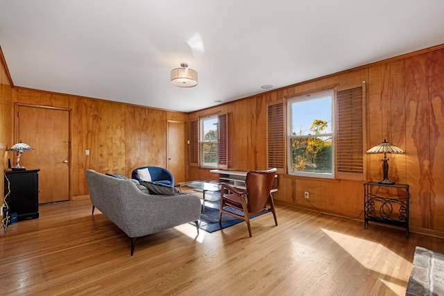 living area featuring light wood-type flooring, a healthy amount of sunlight, and wood walls