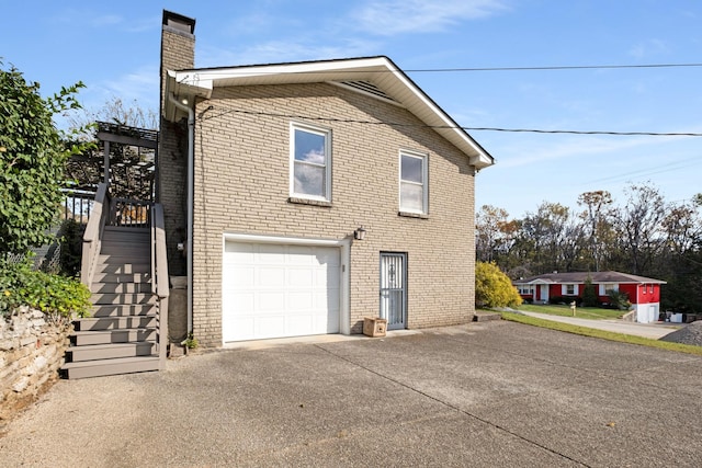 view of side of home featuring driveway, a garage, a chimney, stairway, and brick siding