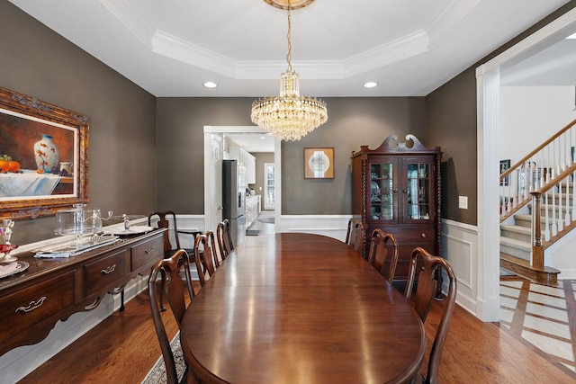 dining room featuring stairs, a tray ceiling, wood finished floors, and wainscoting