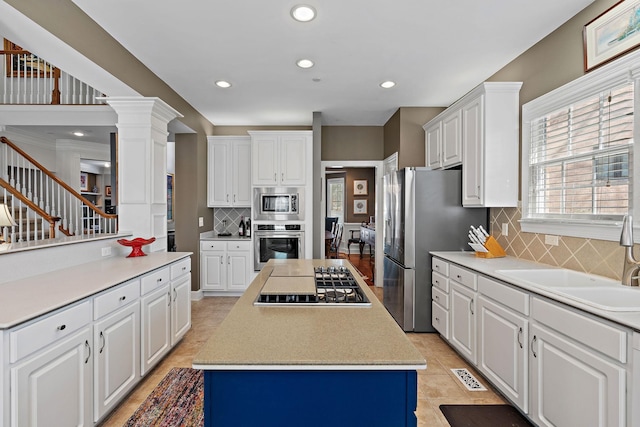 kitchen featuring stainless steel appliances, a sink, white cabinets, a center island, and ornate columns