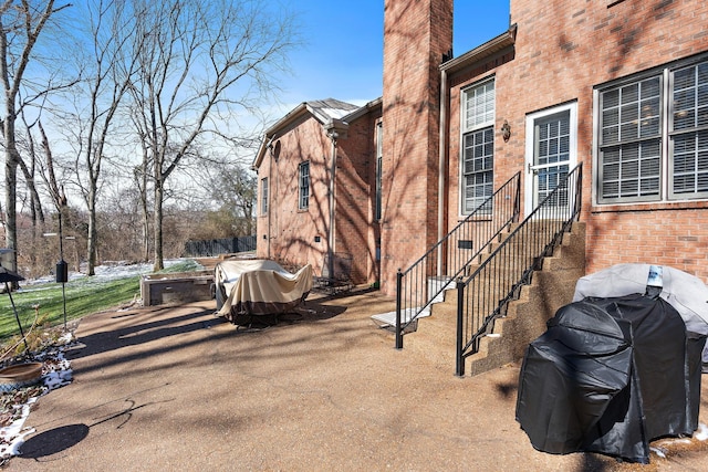 view of side of property featuring entry steps, brick siding, a chimney, and a patio area