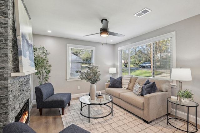 living room with visible vents, baseboards, a glass covered fireplace, light wood-style flooring, and ceiling fan