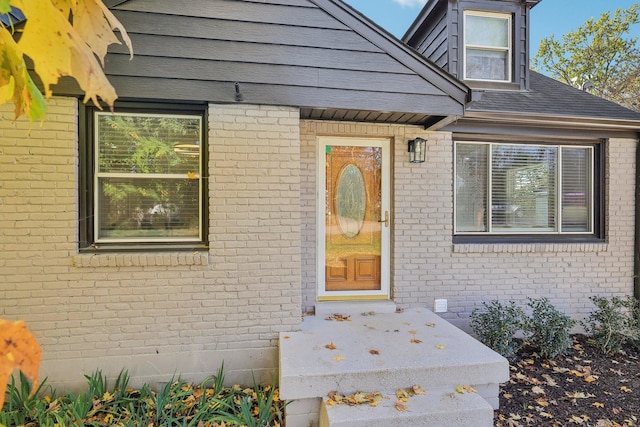 doorway to property with roof with shingles and brick siding