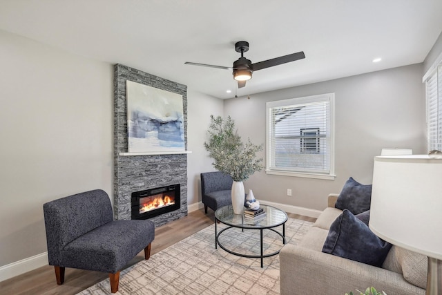 sitting room with light wood finished floors, ceiling fan, baseboards, and a stone fireplace