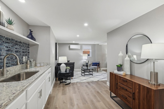 interior space with white cabinets, a wall unit AC, light wood-type flooring, open shelves, and a sink